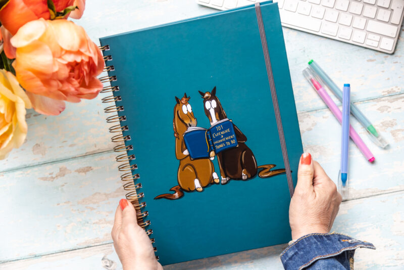 A4 hardback Notebook Two horses reading a book titled '101 expensive and inconvenient things to do'