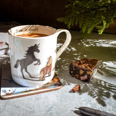 Image of Emily Cole's 'Believe in Yourself' Fine Bone China Mug, featuring a flaxen pony gazing at its unicorn shadow. An inspiring quote ' Believe in yourself' written along the inside rim.