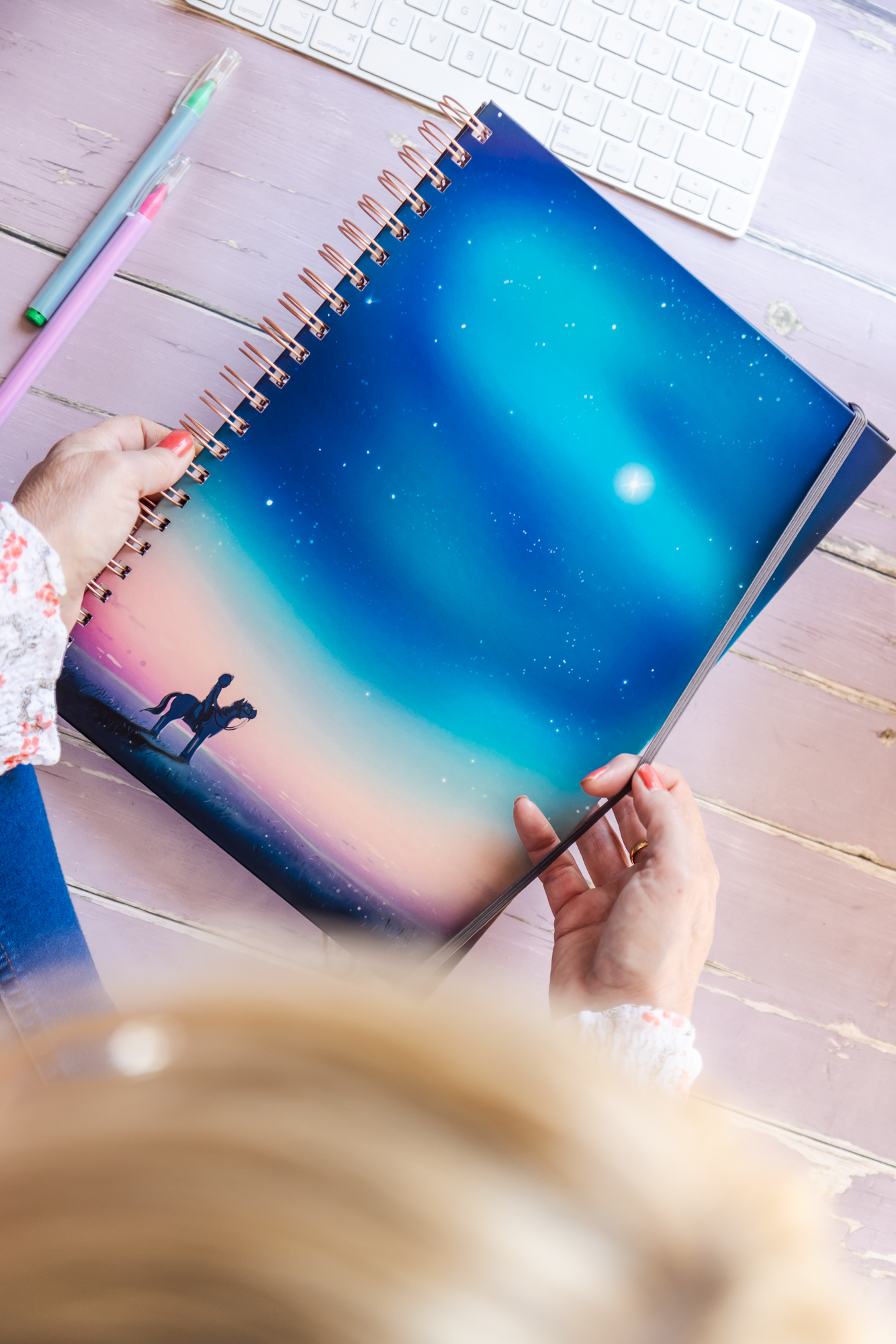 Lady Holding the elastic A4 'Starry Sky' hardback horse notebook. Featuring a horse and rider looking up at a beautiful starry sky aroura.