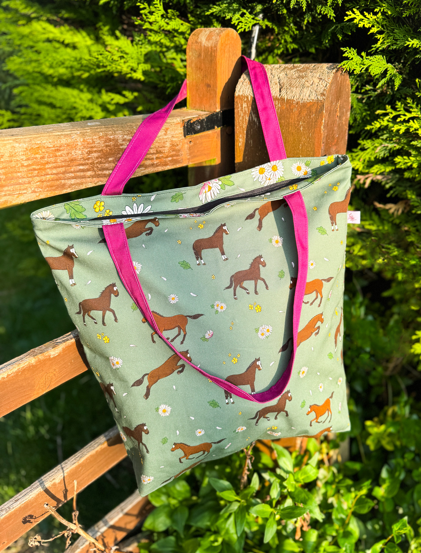 Bay horse patterned oversized tote bag with daisy print and pink straps hanging on a wooden gate