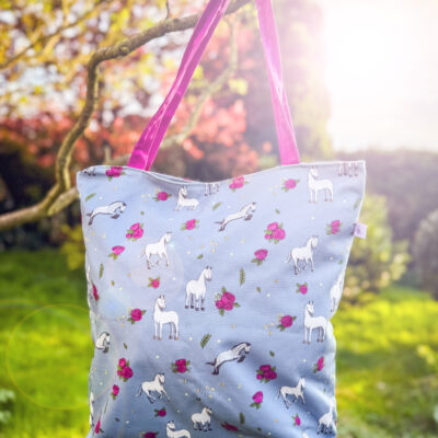Grey horse and rose patterned tote bag hanging from tree with sunlight and pink handles