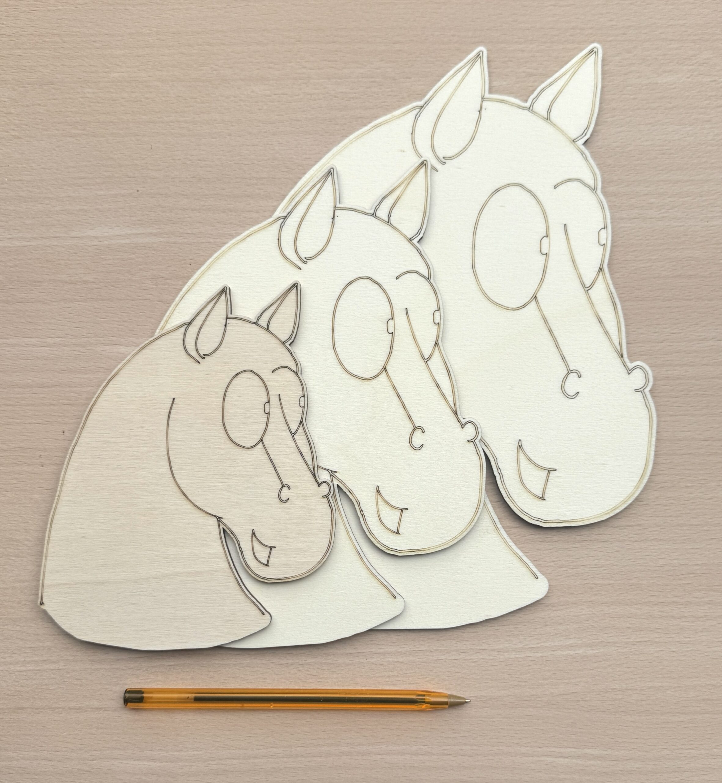 Three unpainted wooden horse heads in small, medium, and large sizes