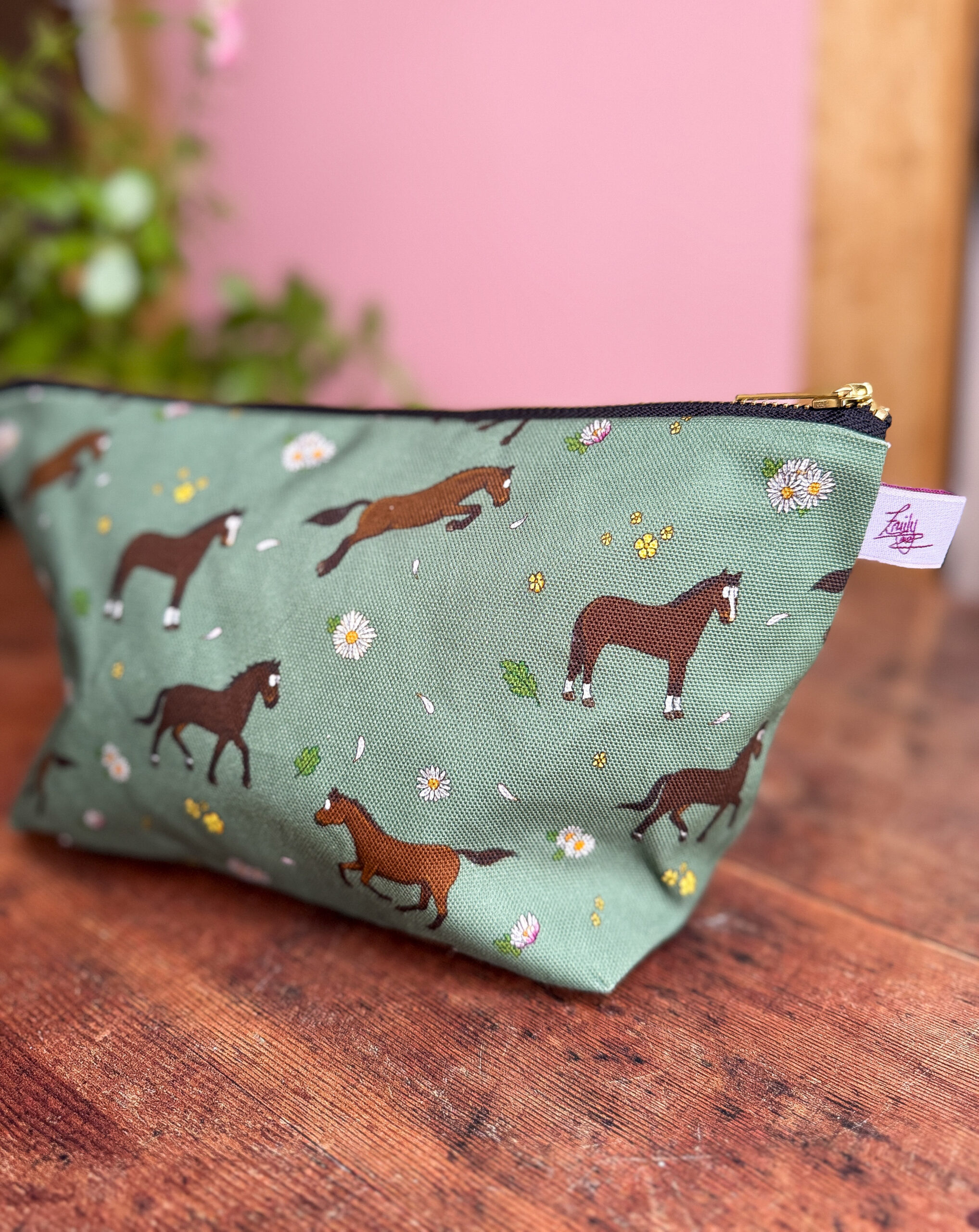 Angled view of bay horse and pony patterned wash bag on wooden surface with soft pink background