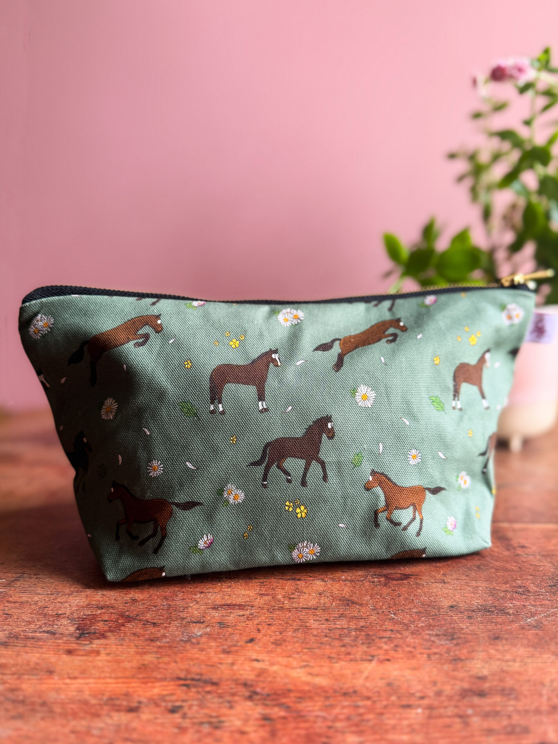 Bay horse and pony patterned wash bag with green background and floral accents, displayed on a wooden surface