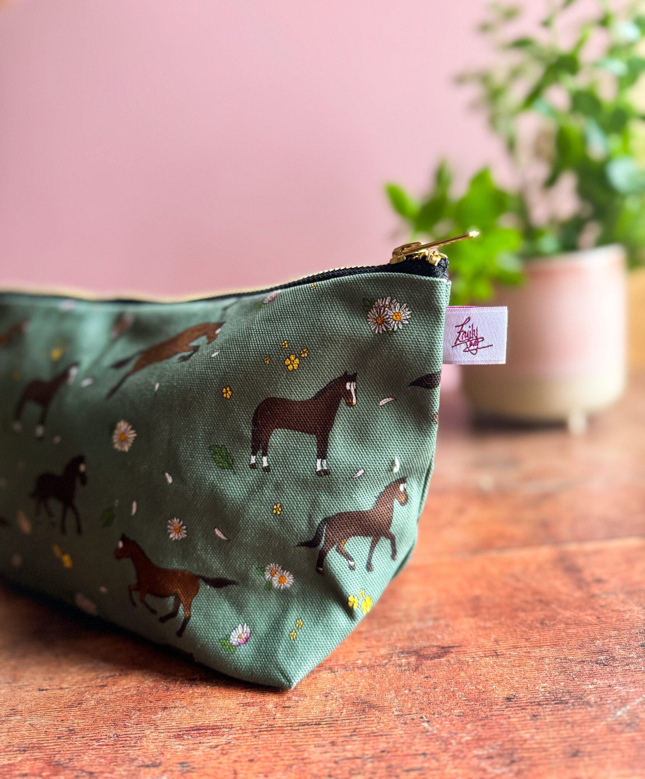 Close-up of horse and daisy pattern on green wash bag with brass zip and designer tag