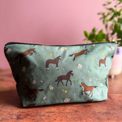 Bay horse and pony patterned wash bag with green background and floral accents, displayed on a wooden surface