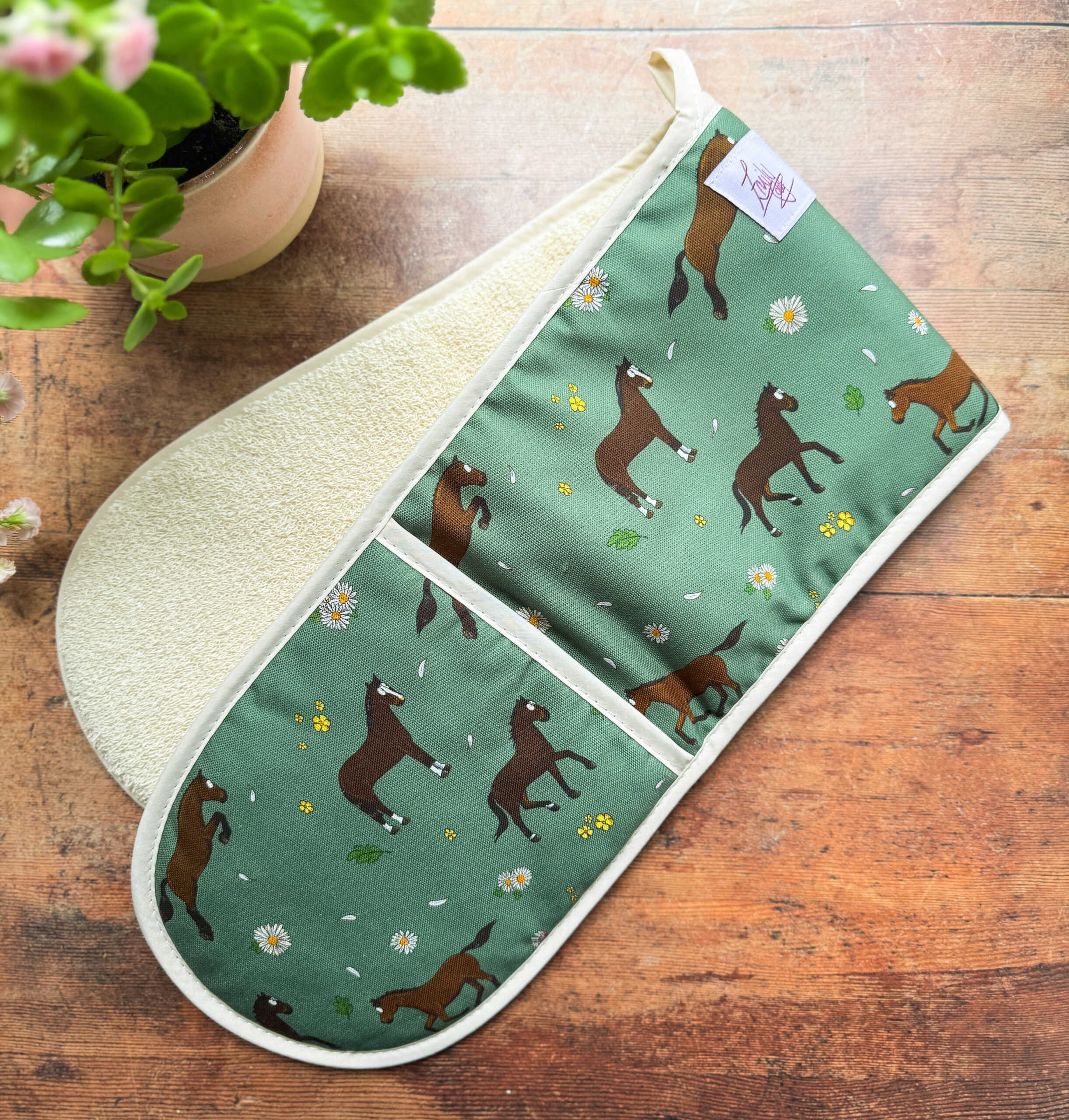 Full view of double oven gloves featuring bay horses and daisy pattern on green background